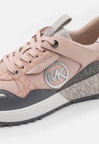 Baskets Michael Kors avec une tige en tissu rose, des accents gris et une semelle compensée texturée. Détail du logo argenté sur le côté.