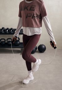 Vaaleanpunainen lyhytnheimainen t-paita, jossa on "NIKE PRO" -logo, kerroksittain valkoisen pitkähihaisen paidan päällä. Tummanpunaiset legginsit ja vaaleat urheilukengät, pitäen hyppynarusta kiinni.