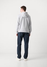 Lys grå hettegenser med en jevn tekstur, kombinert med mørkeblå denimjeans og kremfargede sneakers. Synlige sømdetaljer.