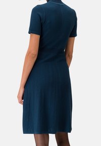 Stickad klänning i mörkblått med figurnära överdel, korta ärmar, texturerade vertikala ränder och en utsvängd kjol. Har en enkel krage.