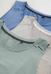 Trois débardeurs de sport sans manches en vert, beige et bleu, fabriqués en tissu mesh respirant, empilés et étalés à plat.