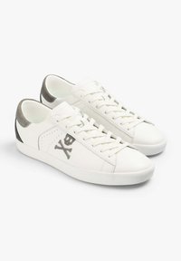Weiße Ledersneaker mit grauen Akzenten, Schnürdesign und subtiler Totenkopf-Grafik an der Seite; glatte Textur und abgerundete Spitze.
