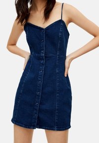 Denim dress with a fitted bodice, adjustable spaghetti straps, and front button closure. Dark blue color with a soft texture and subtle stitching.