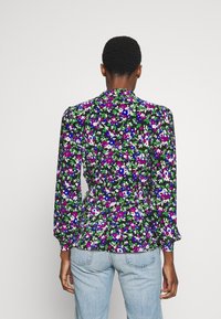 Blommig blus med lång ärm, svart bakgrund, livfulla lila, gröna och vita blommor. Har en peplum midja och krage.