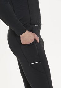 Svart sportkläder med en kroppsnära design, snabbtorkande material och en sidoficka med en reflektiv remsa för synlighet.