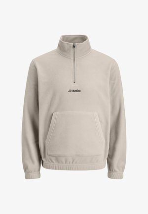 Šviesiai ruda vilnos megzta palaidinė su ketvirčio užtrauktuku, stovinčia apykakle, priekinė kišenė ir siuvinėtas "JJ Studios" logotipas. Minkšta tekstūra ir laisvas kirpimas.