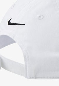 Căciulă albă din bumbac cu vizieră curbă, având un logo Nike negru brodat pe față și o curea reglabilă în spate.