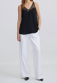 Black sleeveless top with lace detail at the neckline, paired with white wide-leg trousers and pointed black heels. Minimalistic design.