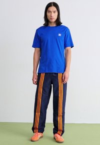 Blå bomulds t-shirt med et lille hvidt logo, parret med navy sweatpants med tre orange striber langs siderne og orange sneakers.