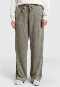 Wijde broek in een gestructureerde, gedempte grijze stof met een tailleband met trekkoord. Afgewerkt met een subtiel patroon en gecombineerd met witte sneakers.
