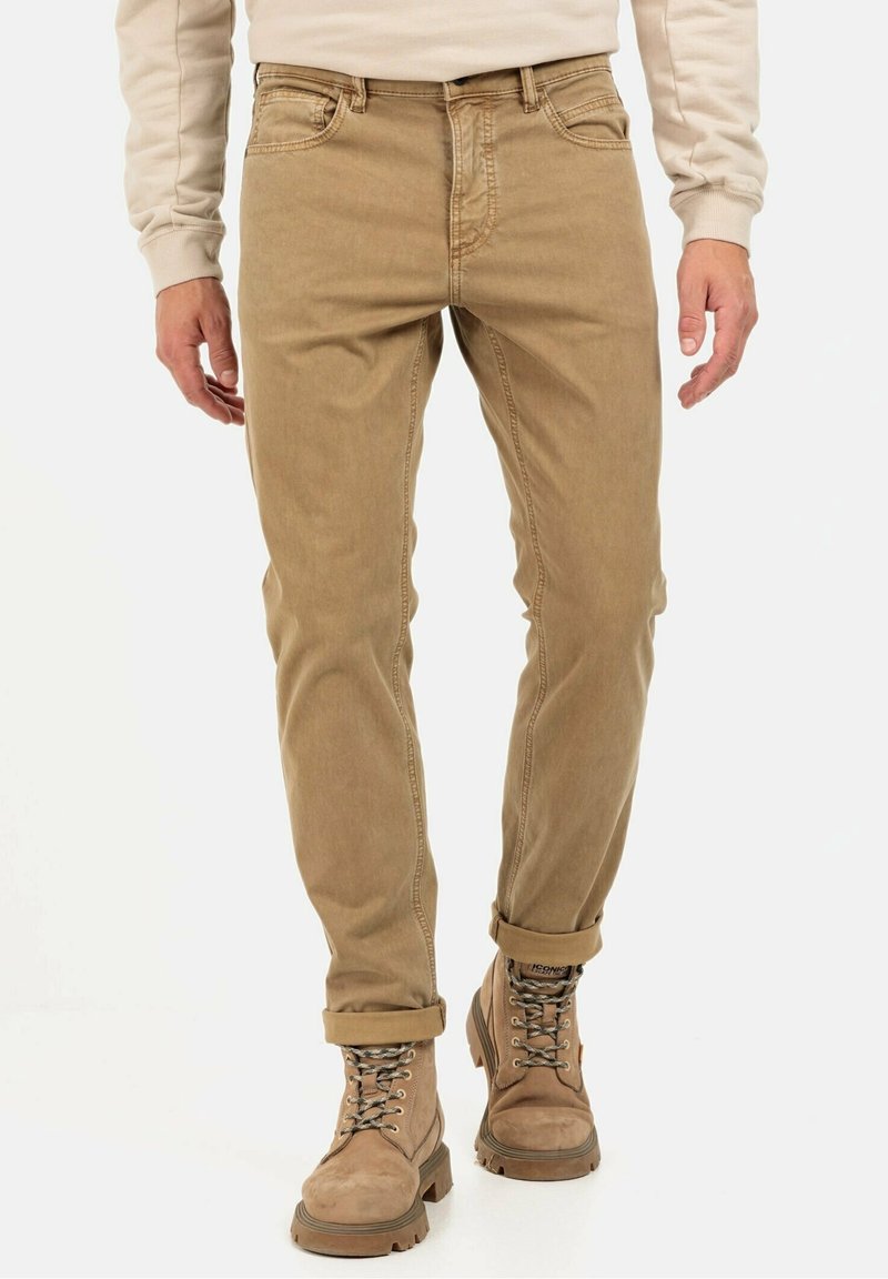 Beige katoenen broek met een slim fit en opgerolde boorden, gecombineerd met lichtbruine leren laarzen met metalen oogjes en veters.