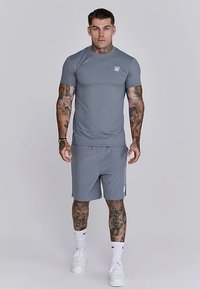 Grå atletisk skjorta och matchande shorts, gjorda av mjukt tyg. Har korta ärmar, en figurnära design och en liten logotyp på bröstet.