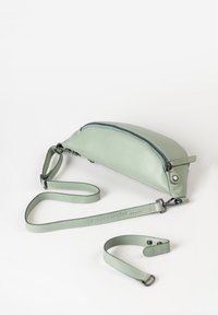 Lichtgroene leren tas met een ronde vorm en een ritssluiting aan de bovenkant. Voorzien van een verstelbare schouderriem en een logo dat op de riem is geperst. Glad textuur.