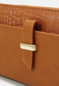 Portefeuille en cuir marron avec un motif crocodile texturé sur le dessus, présentant un accent en métal doré et une finition lisse et mate.