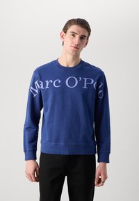 Sudadera de cuello redondo azul marino, mezcla de algodón, con gran texto en color lila "Marc O'Polo" en el frente, puños y dobladillo de canalé.