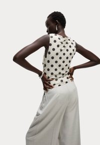 Top senza maniche a pois crema con pois neri, abbinato a pantaloni a gamba larga grigio chiaro, caratterizzati da una vestibilità comoda e una texture liscia.