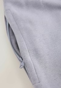 Tissu gris clair avec une fermeture éclair partiellement ouverte, montrant la couture le long du bord de la fermeture éclair.