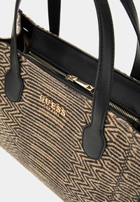 Bruine handtas met een patroon en zwarte leren accenten en handvatten. Voorzien van een ritssluiting en een gouden logo-detail aan de voorkant.