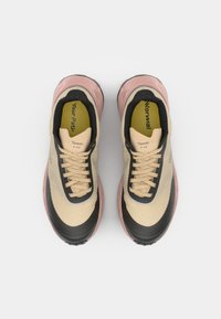 Beige sportieve schoenen met een gestructureerde bovenkant, zwarte accenten, roze tussenzool en zwarte zool. Voorzien van ronde veters en binnenzolen gemarkeerd met "Jouw Pad."