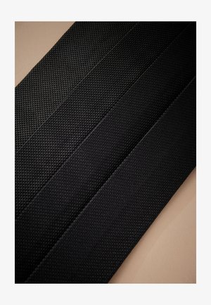 Vier schwarze, strukturierte Stoffriemen oder Gürtel, diagonal auf einem beigefarbenen Hintergrund angeordnet.