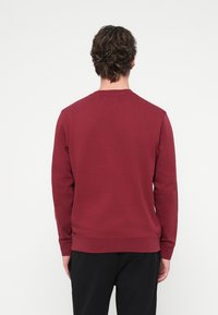 Bordó pulóver kerek nyakkivágással, hosszú ujjakkal, bordázott mandzsettával és szegéllyel. Puha tapintású, egyszínű, látható logó nélküli kialakítás.