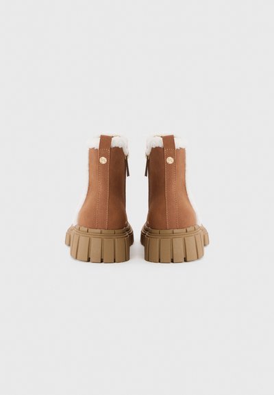 Botas de tornozelo em camurça castanha com forro branco de pelúcia sintética, bico arredondado, sola de borracha texturizada e fecho de zip na parte traseira.