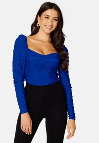 Maglietta a maniche lunghe di colore blu royal con scollatura quadrata e texture arricciata, abbinata a pantaloni neri a vita alta.
