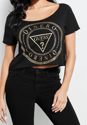 Schwarzes kurz geschnittenes T-Shirt mit einem goldfarbenen kreisförmigen Logodesign, auf dem die Worte "GUESS" und "DINERO" stehen, kurzen Ärmeln und einem weiten Rundhalsausschnitt.