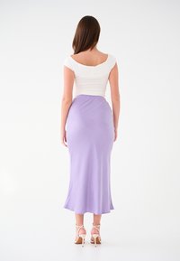 Top bianco aderente con scollatura quadrata abbinato a una gonna midi lavanda. La gonna ha una texture liscia e un orlo fluido. Sono indossati sandali con tacco.