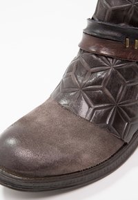 Leren enkellaars in donkergrijs en bruin, met een suède neus, geperst geometrisch patroon en een bruine band met metalen beslag.