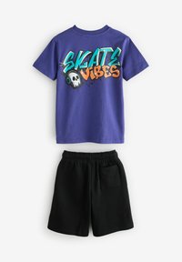 Violetti puuvillapaita, jossa on "SKATE VIBES" -grafiikka, jossa on pääkallo ja kuulokkeet; yhdistetty mustiin elastisiin shortseihin, joissa on tasku.