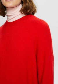 Czerwony dziergany sweter wykonany z miękkiego materiału, z okrągłym dekoltem i lekko oversize'owym krojem, o gładkiej fakturze i minimalistycznych detalach.