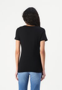 Zwarte T-shirt met korte mouwen en een ronde halslijn, weergegeven vanuit de achterkant, gecombineerd met lichtblauwe jeans.