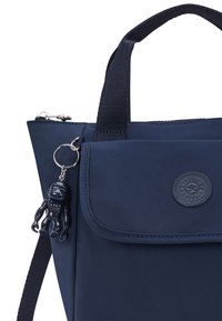 Zaino navy con finitura testurizzata, tasca frontale piatta e logo rotondo. Dotato di un portachiavi rimovibile a forma di piccola figura.
