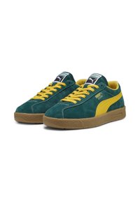 Green suede sneakers with a yellow stripe and laces, featuring a gum rubber sole and a branded tongue tag. Classic low-top design.