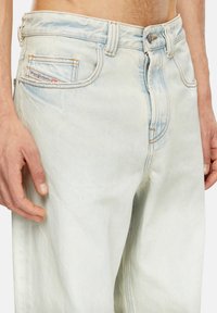 Jean en denim bleu clair avec une coupe décontractée, fermeture à bouton, décoloration subtile, coutures piquées et un petit label logo sur la poche avant.