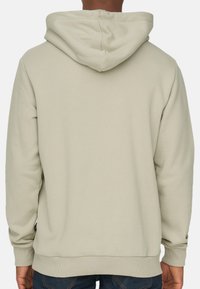 Felpa con cappuccio di un beige chiaro realizzata in tessuto morbido, presenta polsini e orlo a costine, con un design a tasca a marsupio nella parte frontale.