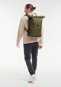 Zaino roll-top in verde oliva, realizzato in materiale resistente. Presenta una tasca frontale con zip, spallacci regolabili e dettagli colorati.