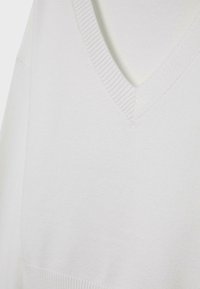 Pull en maille blanc avec un col en V, des côtes texturées au niveau de l'encolure et une finition lisse sur tout le tissu.