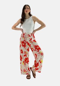 Bloemrijke wijde broek in het wit met rode en gele bloempatronen; elastische tailleband; gecombineerd met een simpele witte tanktop en bruine sandalen.