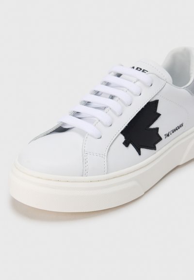 Baskets en cuir blanc avec un dessin de feuille d'érable noire, lacets plats blancs et semelle en caoutchouc texturée. Style minimaliste et finition lisse.