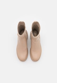 Botas altas de cuero beige con punta redonda, paneles laterales elásticos y suela plana de goma. Textura lisa con diseño minimalista.