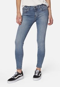 Jeans ajustados azul claro con un ligero desvanecimiento, diseño de cinco bolsillos y trabillas para cinturón, combinados con zapatillas bajas en blanco y negro.