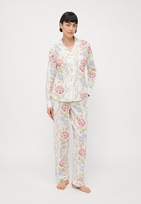Pysjamasett med blomsterdesign som inkluderer en skjorte med knapper og matchende bukser. Fargene inkluderer rosa, blå og grønn på en kremfarget bakgrunn.