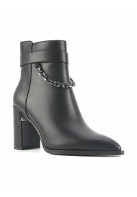 Black ankle boot made of textured leather, featuring a pointed toe, chunky heel, and a chain accent around the ankle. Minimalist design.