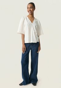 White puff-sleeve blouse with textured pattern, paired with flared dark denim jeans featuring prominent stitching and a high waist.