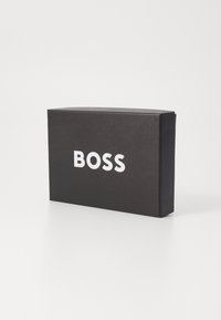 Scatola di cartone nera con finitura opaca, caratterizzata da grandi lettere bianche che scrivono "BOSS" sul fronte. Forma rettangolare con bordi netti.