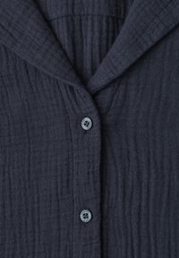 Dark gray textured shirt fabric with two visible buttons and a folded collar, showing vertical stitched lines on the material.