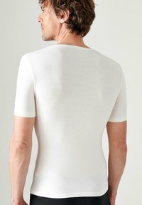 Witte fitted shirt met korte mouwen, geribbelde textuur, ronde halslijn, gladde stof, minimaal design, gedragen door een mannelijke model vanuit een achteraanzicht.