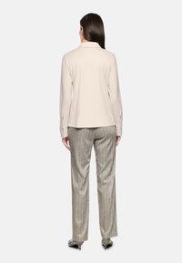 Beige collared blouse with long sleeves and a relaxed fit, paired with gray pinstripe trousers. Smooth texture and tailored design.